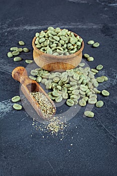 Raw green unroasted coffee in wooden bowl with ground beans in wood scoop