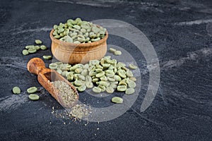 Raw green unroasted coffee in wooden bowl with ground beans in wood scoop