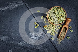 Raw green unroasted coffee in wooden bowl with ground beans in wood scoop on black slate board