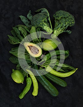 Raw green vegetables set. Broccoli, avocado, pepper, spinach, zucchini, lime on dark stone background