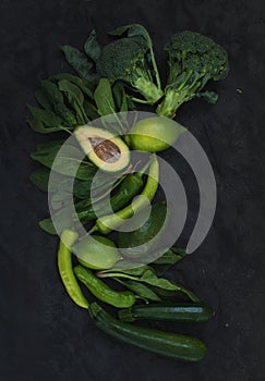 Raw green vegetables set. Broccoli, avocado, pepper, spinach, zuccini and lime on dark stone background