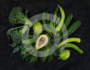 Raw green vegetables set. Broccoli, avocado, pepper, spinach, zuccini and lime on dark stone background