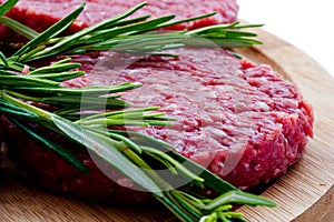 Raw hamburgers with cellophane and rosemary on wooden board