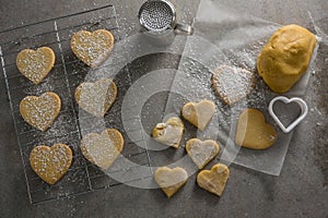 Raw heart shape cookies on baking tray with flour shaker strainer, cookie cutter and wax paper