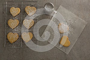 Raw heart shape cookies on baking tray with flour shaker strainer and wax paper