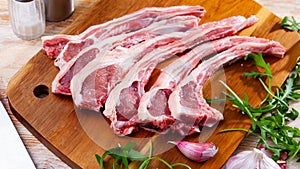 Raw hogget chops on wooden board with arugula and garlic