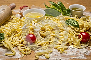 Raw homemade pasta with fresh herbs , tomatoes, flour, rolling pin ,egg and olive oil on rustic wooden background close up