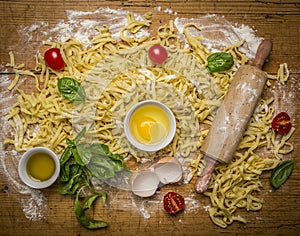 Raw homemade pasta with ingredients for pasta, tomatoes, flour, rolling pin ,egg and olive oil on rustic wooden background top vi