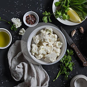 Raw ingredients - cauliflower, olive oil, herbs, lemon and spices on a dark background