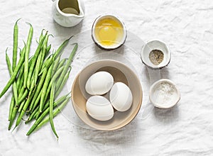 Raw ingredients for cooking breakfast - eggs, green beans, olive oil, spices on a white background, top view.