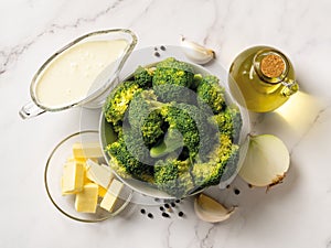 Raw ingredients for cooking cream of broccoli soup: broccoli florets, cream, butter, garlic, onion and olive oil. Puree soup of