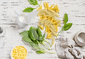 Raw ingredients for making pasta with spinach cream sauce - penne pasta, fresh spinach, cream, cheese and spices on a wooden