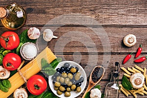 Raw ingredients for the preparation of Italian pasta, spaghetti, basil, tomatoes, olives and olive oil on wooden