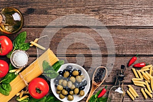 Raw ingredients for the preparation of Italian pasta, spaghetti, basil, tomatoes, olives and olive oil on wooden