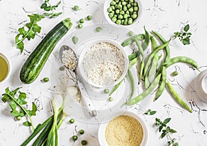 Raw ingredients - rice, cous cous, zucchini, green beans and peas, olive oil on a light background.