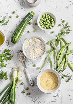 Raw ingredients - rice, cous cous, zucchini, green beans and peas, olive oil on a light background.