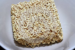 Raw instant noodles squares shape closeup in the white bowl. it is in a precooked and dried noodle block.
