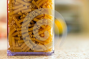 Raw italian macaroni pasta inside clear storage container