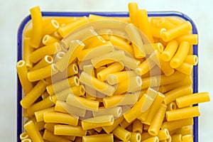 Raw italian macaroni pasta inside clear storage container