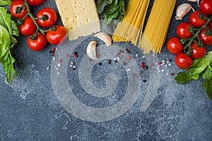 Raw Italian pasta spaghetti and cooking ingredients cherry tomatoes Cheese greens. Italian food dark stone background. Top view