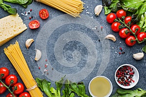 Raw Italian pasta spaghetti and cooking ingredients cherry tomatoes Cheese greens. Italian food dark stone background. Top view