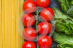 Raw Italian pasta spaghetti and cooking ingredients cherry tomatoes greens. Italian food dark stone background. Top view with copy