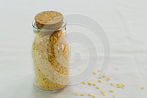 Raw Italian risoni pasta in a glass jar on a table. The concept of traditional cuisine. Vertical orientation.