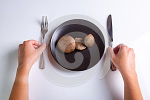 Raw Jersey cow mushrooms in a black plate and a knife and fork nearby on a white background top view. Human hands