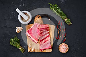 Raw lamb breast ribs on wooden cutting board with herbs and seasoning