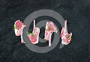 Raw lamb chops. Rack of Lamb with rosemary and spices over black slate stone background.