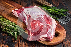 Raw lamb or goat shoulder meat on the bone on a wooden butcher cutting board with cleaver. Dark wooden background. Top