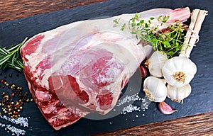 Raw lamb leg on blue stone background with herbs