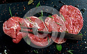 Raw Lamb leg steaks on stone chopping board with vintage fork served with sea salt and chillie flakes, rosemary and mint