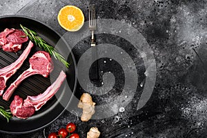 Raw lamb meat chops steaks, on frying cast iron pan, on black dark stone table background, top view flat lay, with copy space for