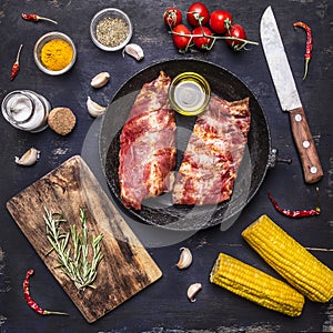 Raw lamb ribs in a cast iron skillet, with a knife for meat, spices and herbs and corn wooden rustic background top view