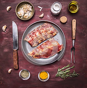 Raw lamb ribs on a frying pan, with a knife and fork for the meat, spices and herbs wooden rustic background top view