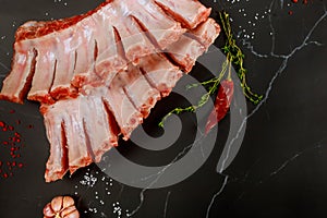 Raw lamb ribs with herbs, garlic and pepper on black background