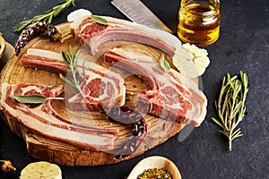 Raw lamb ribs with ingredients for cooking: salt, pepper, olive oil and herbs on a wooden stand