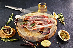 Raw lamb ribs with ingredients for cooking: salt, pepper, olive oil and herbs on a wooden stand