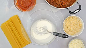 Raw lasagna noodles, ground beef on frying pan, marinara, and cheese in bowls