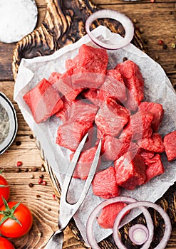 Raw lean diced casserole beef pork steak on chopping board with vintage fork on wooden background. Salt and pepper with fresh