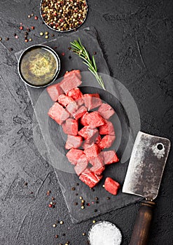 Raw lean diced casserole beef pork steak on chopping board with vintage meat hatchet on stone background. Salt and pepper with