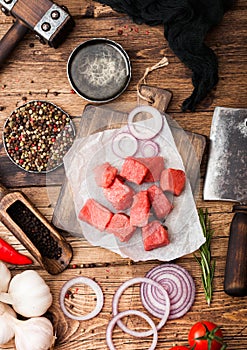 Raw lean diced casserole beef pork steak on chopping board with vintage meat hatchet on wooden background. Salt and pepper with