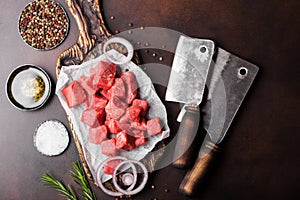 Raw lean diced casserole beef pork steak on chopping board with vintage meat hatchets on brown background. Salt and pepper with
