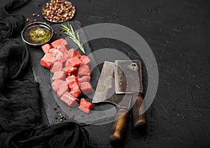 Raw lean diced casserole beef pork steak on chopping board with vintage meat hatchets on stone background. Salt and pepper with