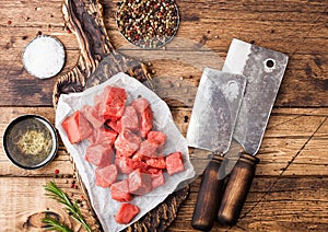 Raw lean diced casserole beef pork steak on chopping board with vintage meat hatchets on wooden background. Salt and pepper with