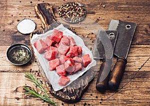 Raw lean diced casserole beef pork steak on chopping board with vintage meat hatchets on wooden background. Salt and pepper with