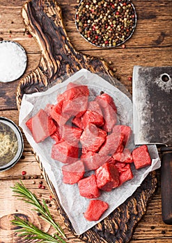 Raw lean diced casserole beef pork steak on chopping board with vintage meat hatchets on wooden background. Salt and pepper with