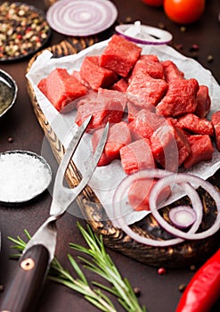 Raw lean diced casserole beef pork steak with vintage meat hatchet and fork on brown background. Salt and pepper with fresh