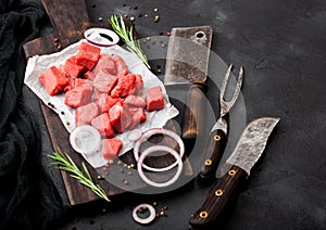 Raw lean diced casserole beef pork steak with vintage meat hatchet and fork with knife on stone background. Rosemary with red